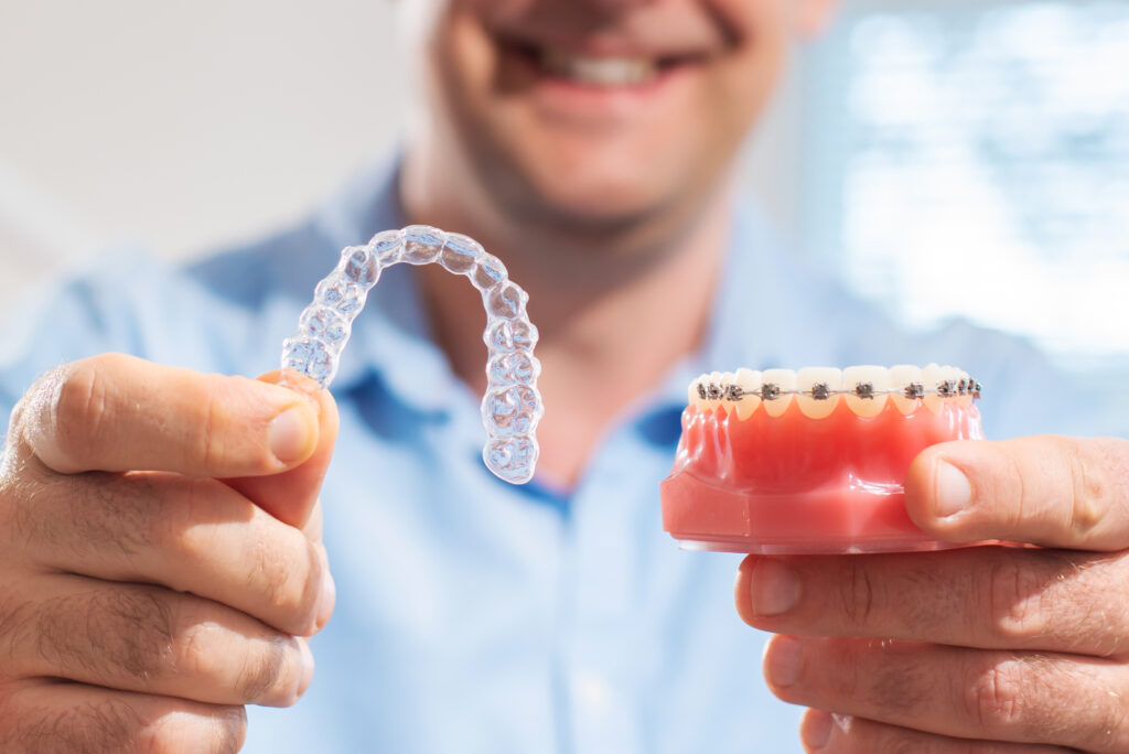 Dentist holding up Invisalign clear aligners & typodont with braces at Global Smiles Dental in Indianapolis, Indiana 46237
