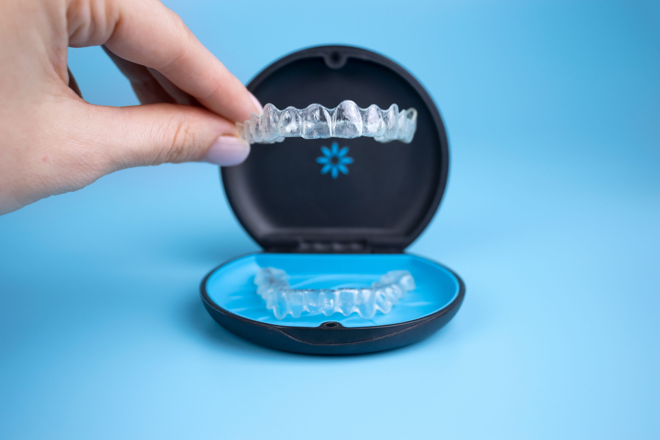 Woman holding invisalign transparent retainers with a box on the table, flatlay top view at Global Smiles Dental in Indianapolis